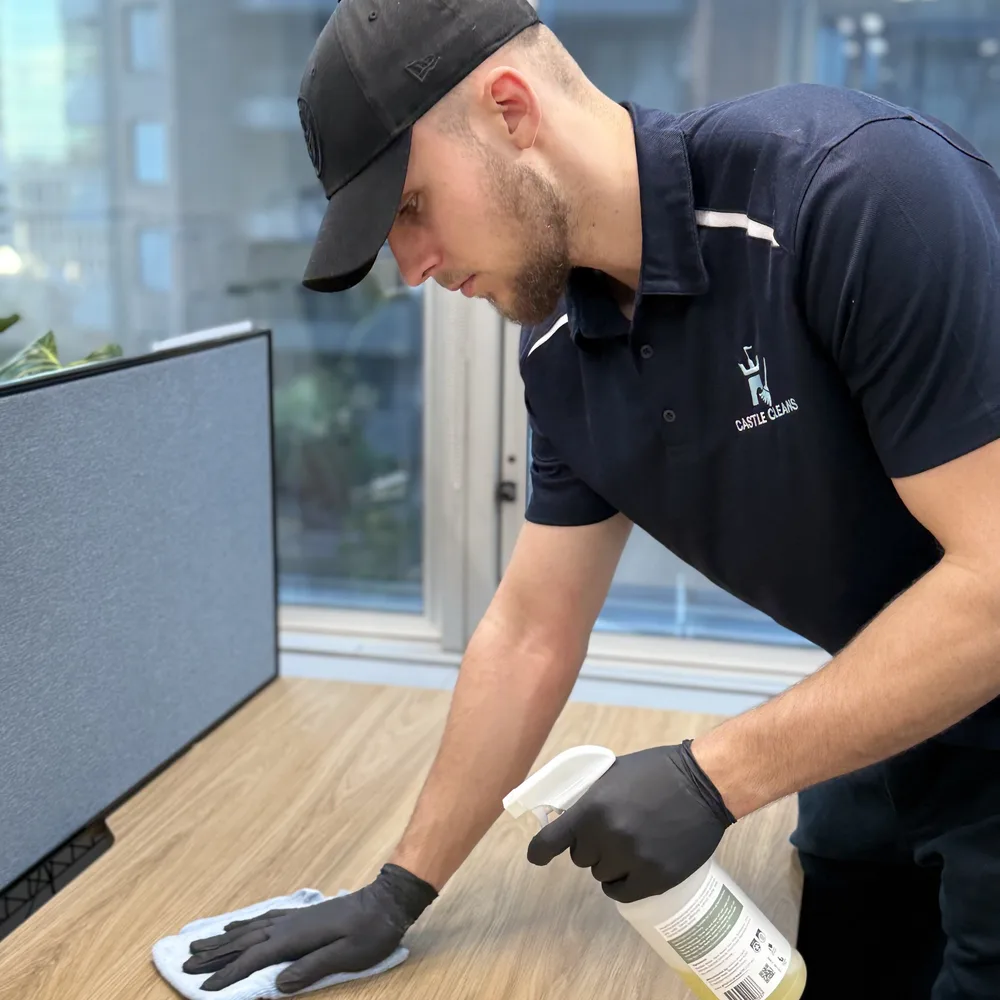 Ryan from Castle Cleans wiping down a desk in a Sydney office, in branded uniform and gloves